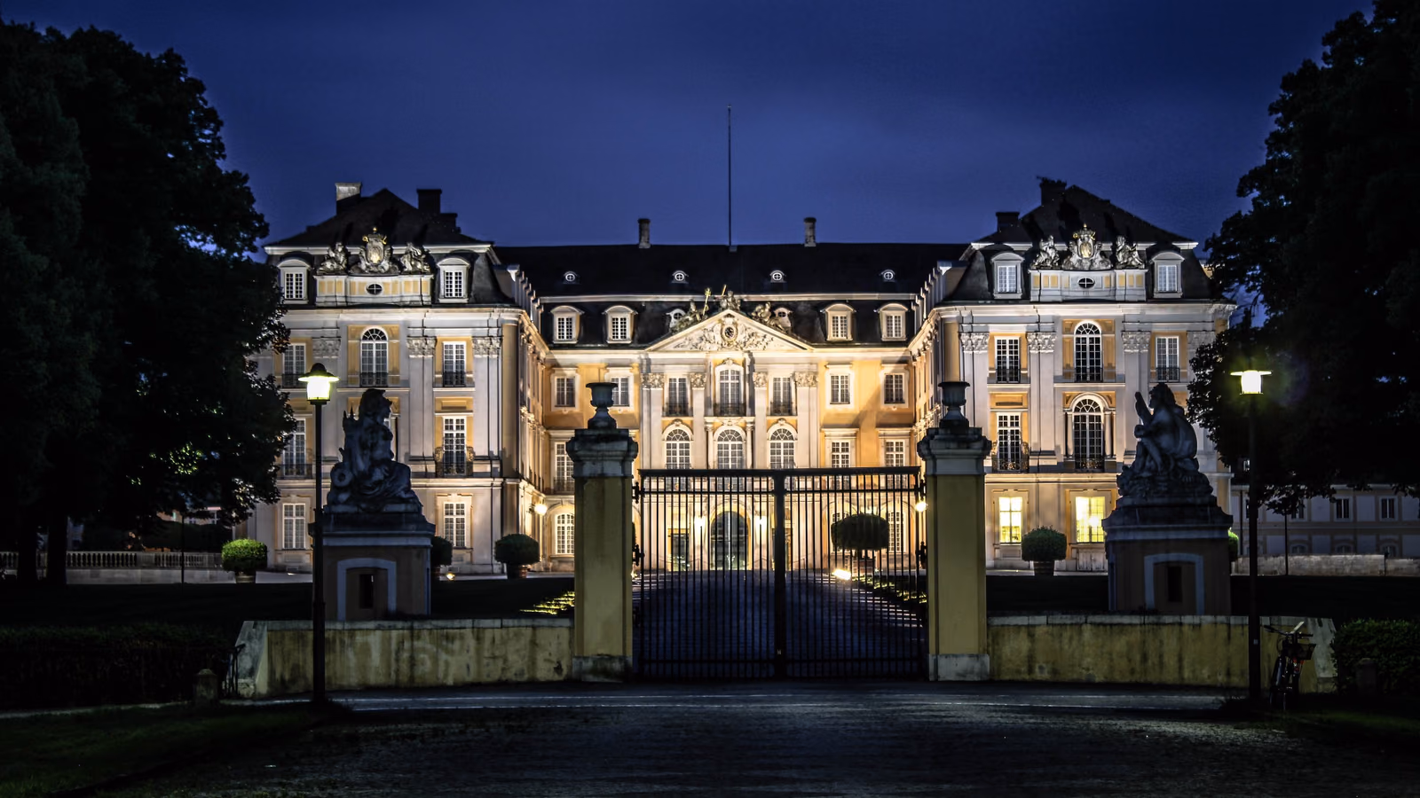 Schloss Augustusburg in Brühl bei Nacht, beleuchtete Fassade hinter dem schmiedeeisernen Tor